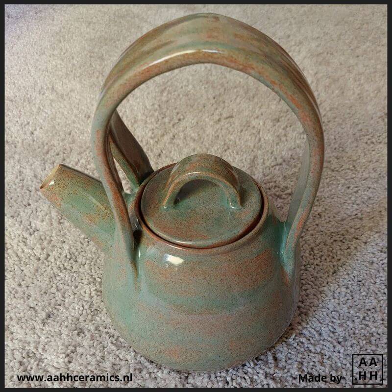 Zelfgemaakte theepot van keramiek met groot en hoog hengsel, geglazuurd met de groene basisvariant van het glazuur waarmee ik heb geexperimenteerd. Waar de glazuur dunner is kleurt hij meer oranje.