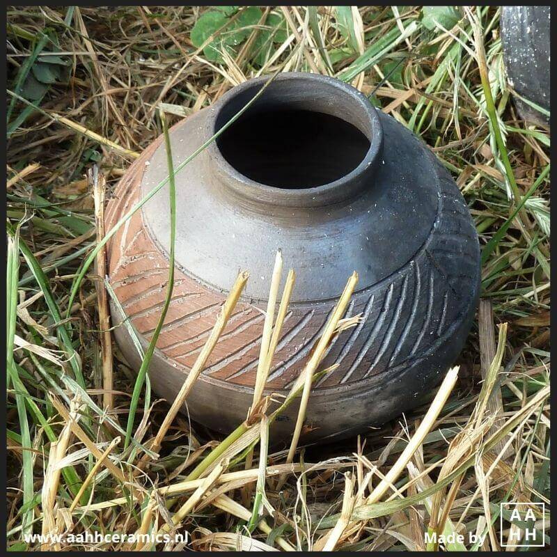 Minivaasje met volle buik en smalle hals met rand met slibdecoratie koelt af in het gras - stook in open houtvuur