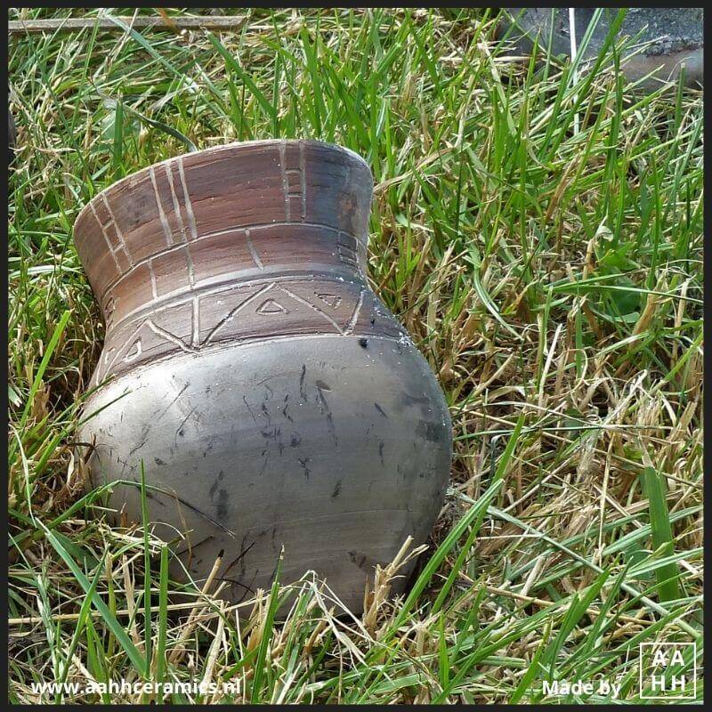 Vaasje met wijdere hals met slibdecoratie ligt af te koelen in het gras - stook in open houtvuur
