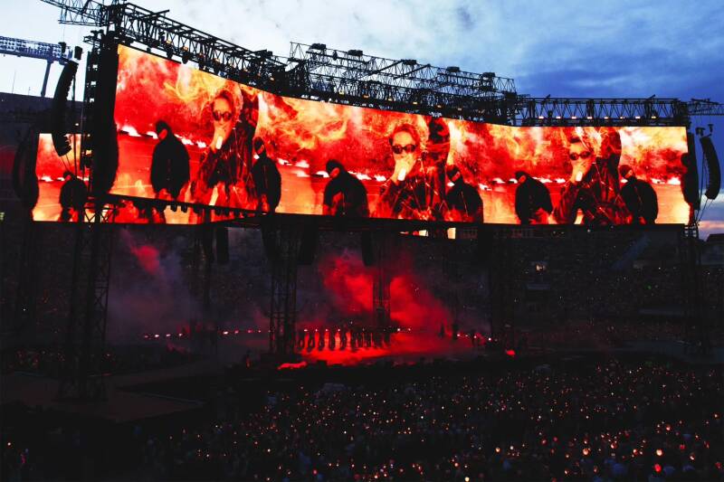 Gran escenario de concierto con pantallas gigantes en tonos rojos y una multitud de fans iluminando el lugar.