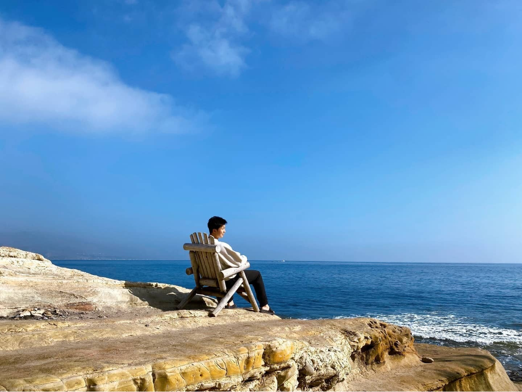 RM de BTS sentado en una silla de troncos de madera frente al mar