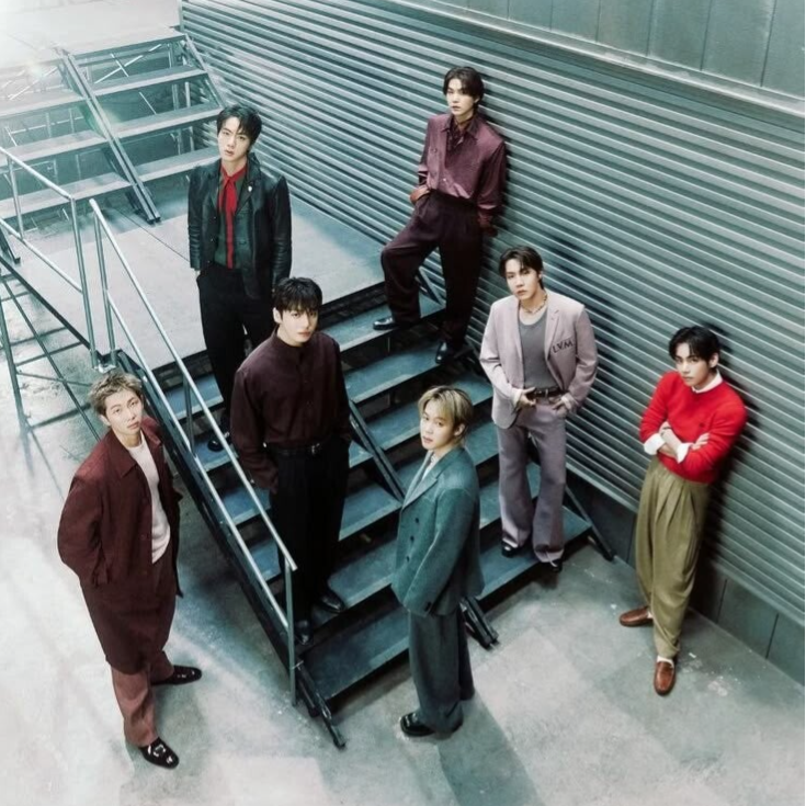 BTS is back. Integrantes posando de pie en unas escaleras, con la cabeza inclinada mirando hacia arrba. Foto en picada.