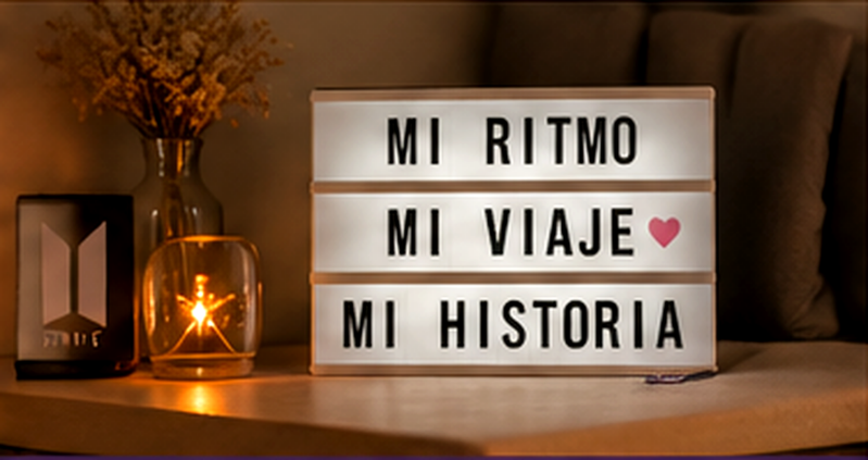 Caja de luz con el mensaje “Mi ritmo, mi viaje, mi historia”, junto a una vela encendida en un ambiente cálido y acogedor. Imagen creada con IA