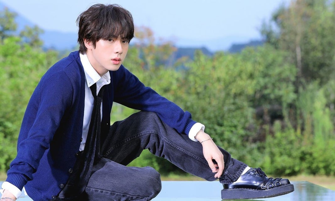 Jin de BTS sentado en un bosque