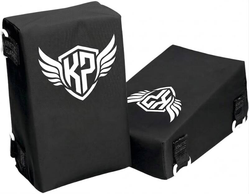 Leg guard pair in black, wedge-shaped with a shield logo, on a white background.