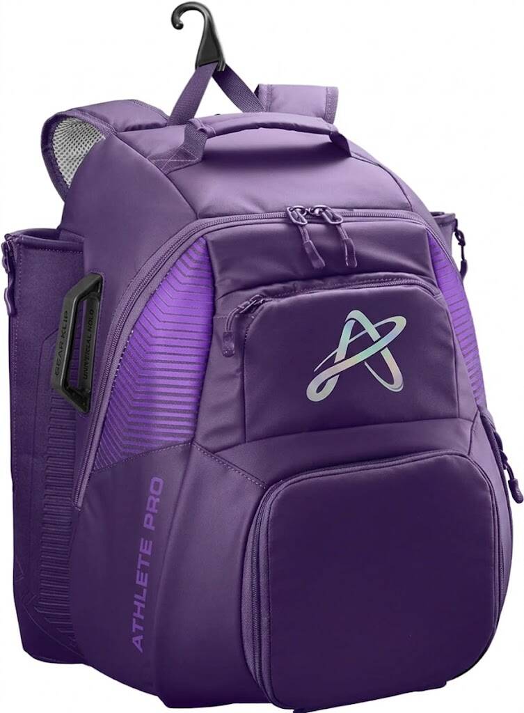 A detailed three-quarter view of a purple and silver baseball equipment backpack on a white background, featuring multiple zippered compartments, a front shield logo, and a side sleeve with a geometric diamond pattern.