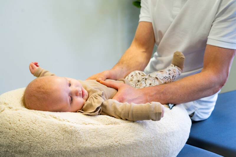 Een baby osteopaat onderzoekt de borstkas van een baby op spanningen die gerelateerd zijn aan een (korte) tongriem.