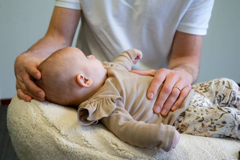 Een baby osteopaat voert een gerichte beoordeling uit van de nek- en borstspanning bij een baby ter behandeling van een voorkeurshouding