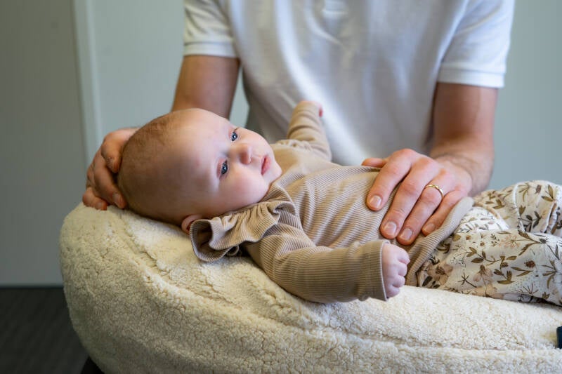 Een baby  osteopaat behandelt de nek en borstkas van een baby om spanningen rondom een korte tongriem te verlichten
