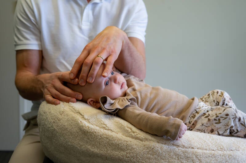 Een baby osteopaat behandelt met zachte hand het hoofdje van een baby om een voorkeurshouding te verhelpen