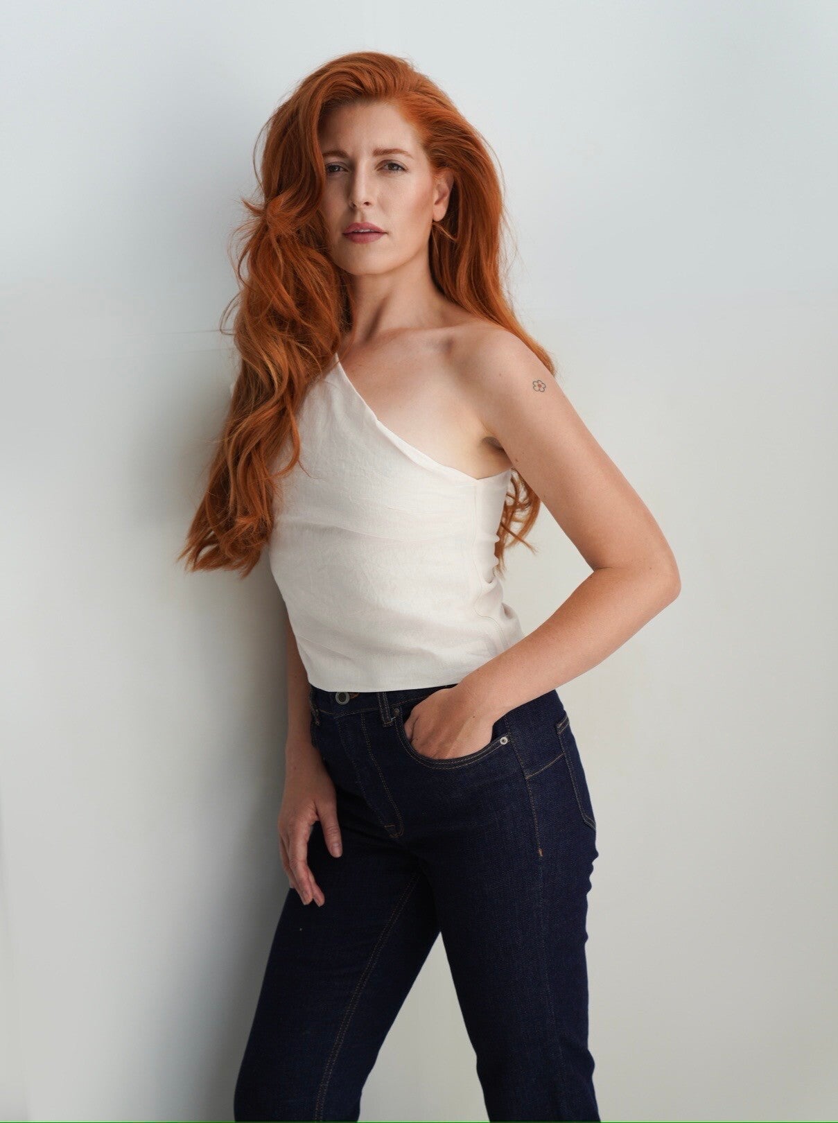 Fashion-forward woman with striking red hair, wearing matching green outfit, sitting casually and looking assertively into the lens against a plain backdrop.