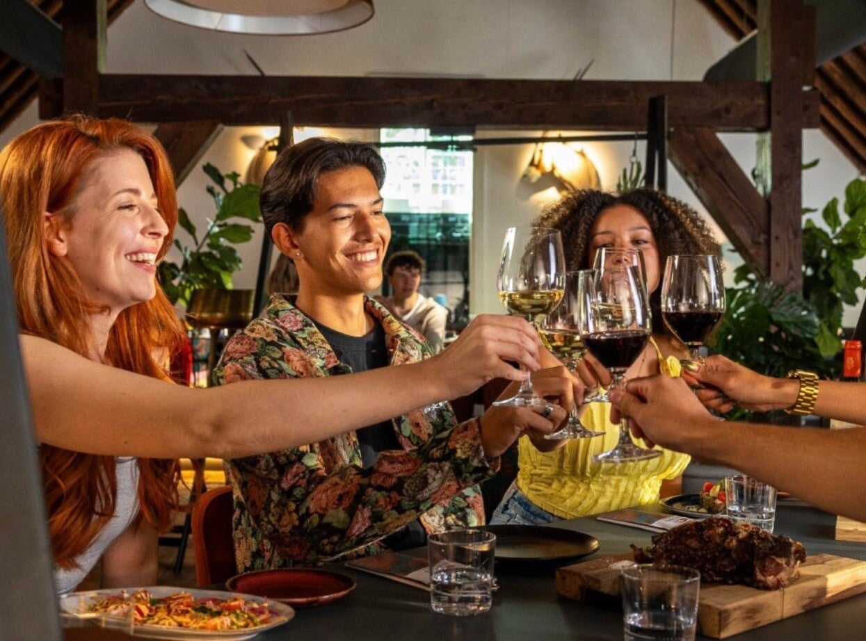 Group of diverse friends celebrating with wine glasses in a cozy restaurant setting, smiling and toasting each other.