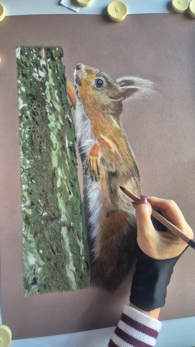 A close‑up of a drawing in progress on pastelmat paper, with pastel pencils scattered around the edges.