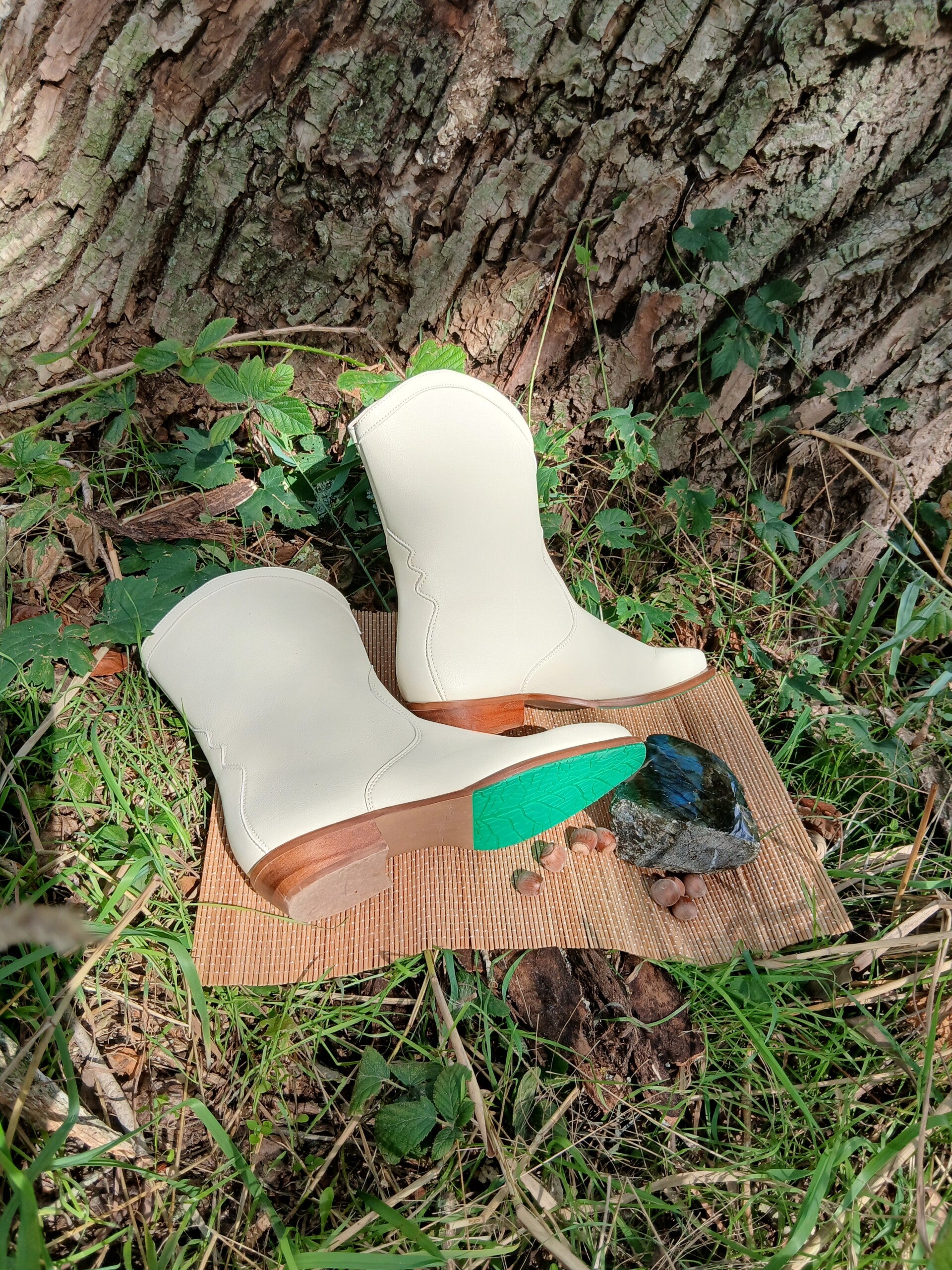 Duurzame witte vegan designlaarzen met een kenmerkende groene zool op een natuurlijke ondergrond, symbool voor geaard en diervriendelijk leven.  