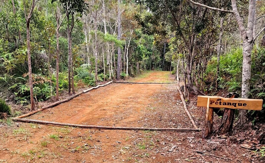 Espace de pétanque en terre battue entouré de rondins de bois au cœur de la propriété