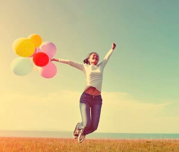 Vrouw springt in de lucht met ballonnen en oogt blij en vrij