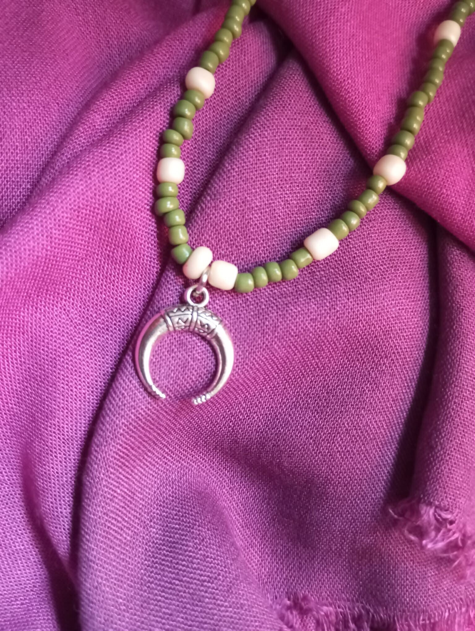 Collar colgante plateado con detalles verdes y blancos.