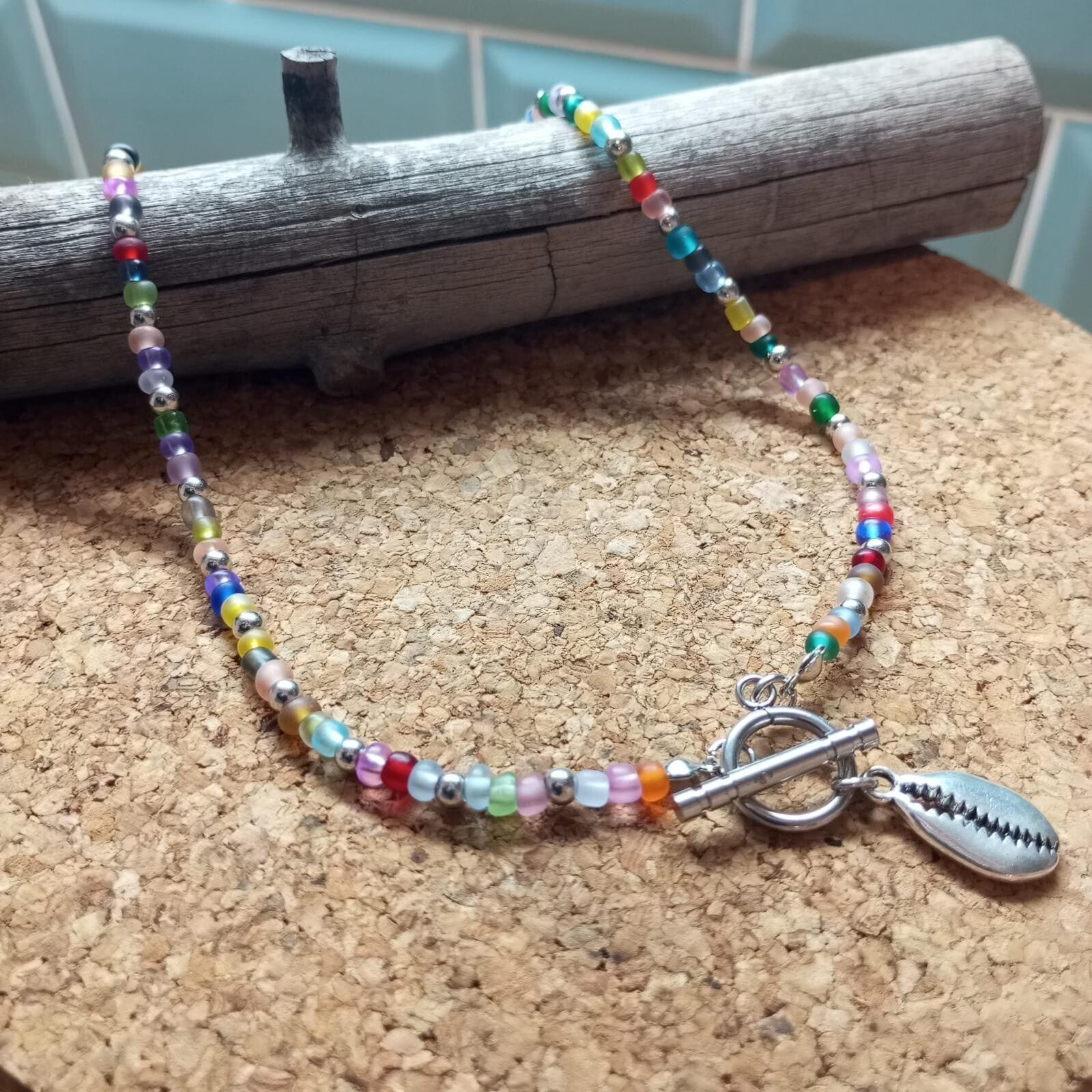 Collar con cuentas de cristal, con detalle de caracola plateada y cierre delantero.