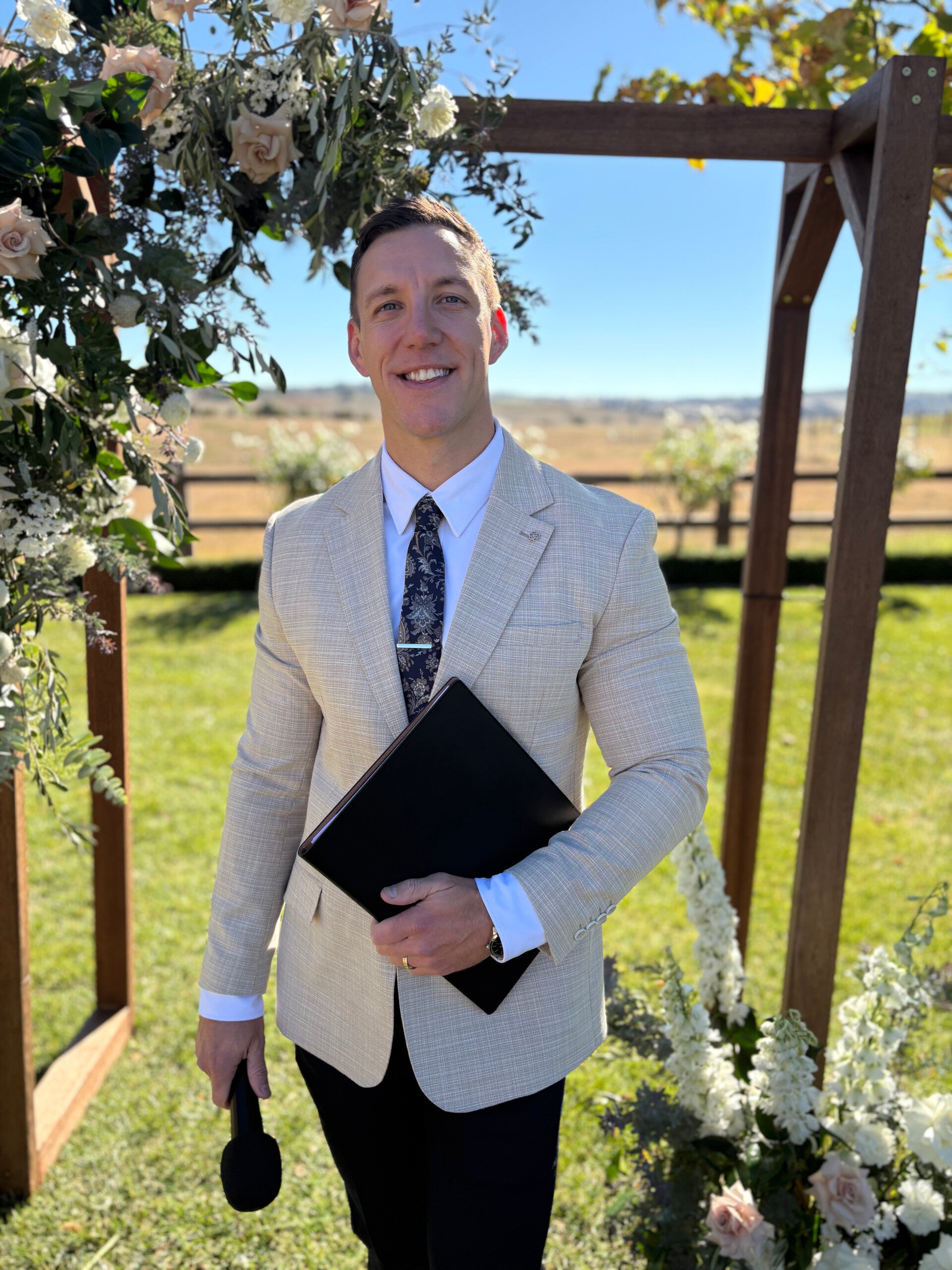 Sydney marriage celebrant Riley Farlow standing beneath floral wedding arbour