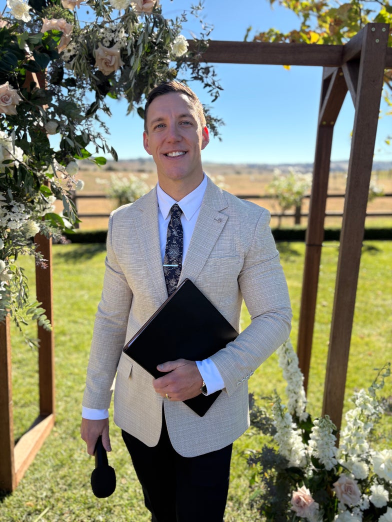 Riley Farlow standing at a wedding ceremony with microphone and folder