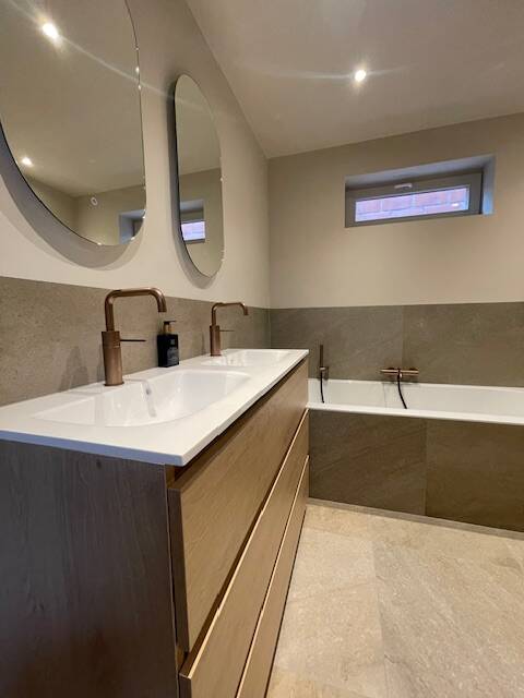 Badkamer met grote spiegel boven dubbele lavabo en indirecte LED-verlichting