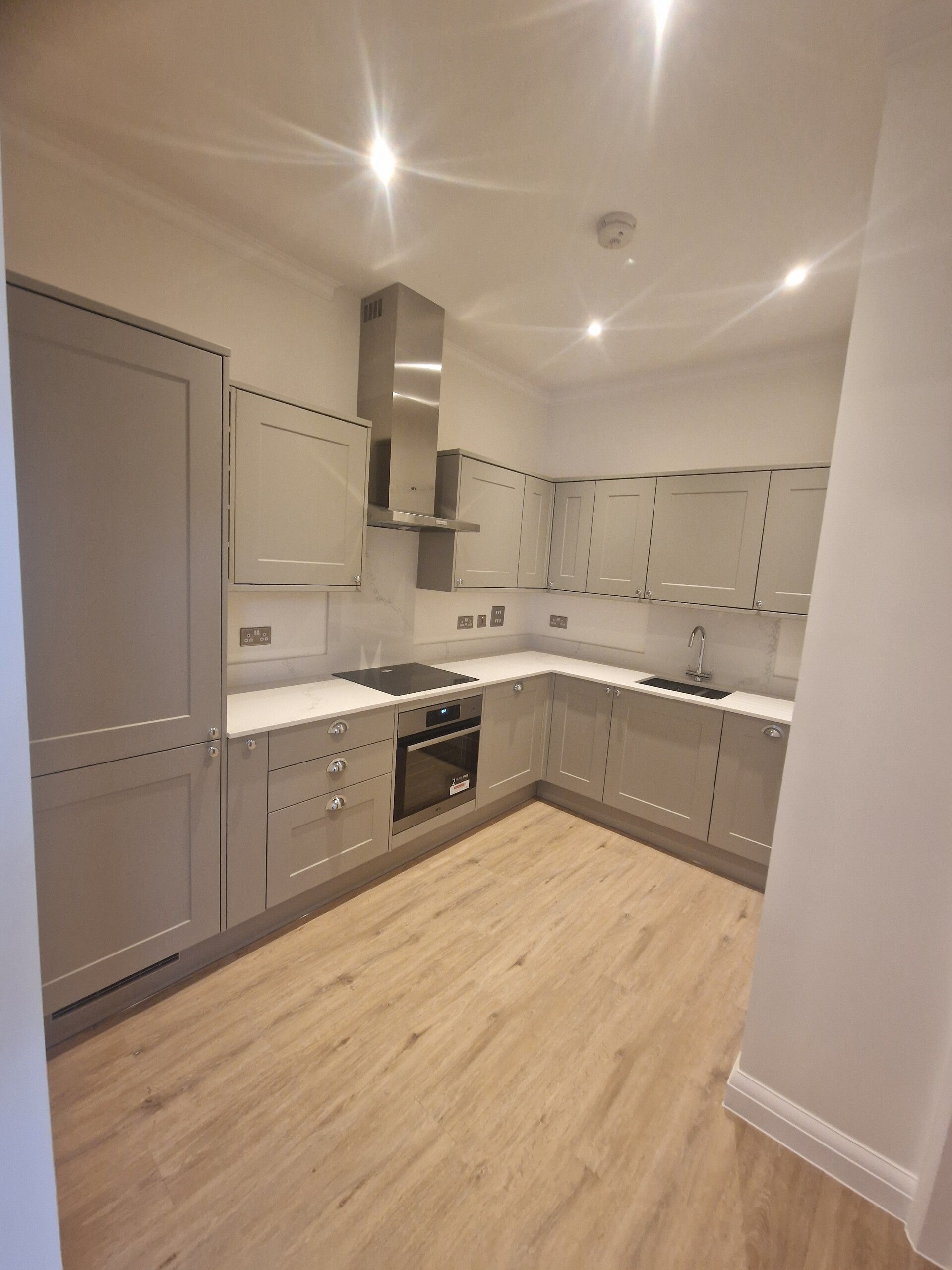 Fitted kitchen with grey cabinets, white worktops and wood-effect flooring