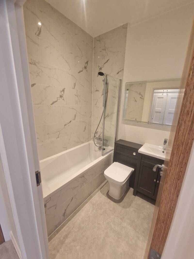 Refurbished bathroom in a Horsham flat with bath and marble-effect wall finish
