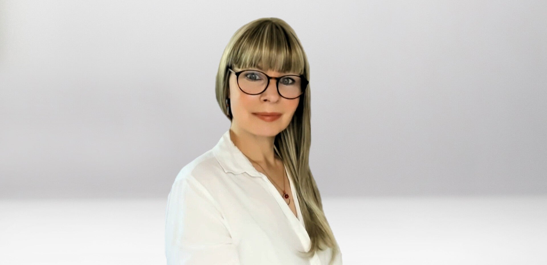 Jana Lorenz mit langen blonden Haaren, trägt weiße Bluse und goldene Ohrringe, Halskette mit rundem roten Anhänger