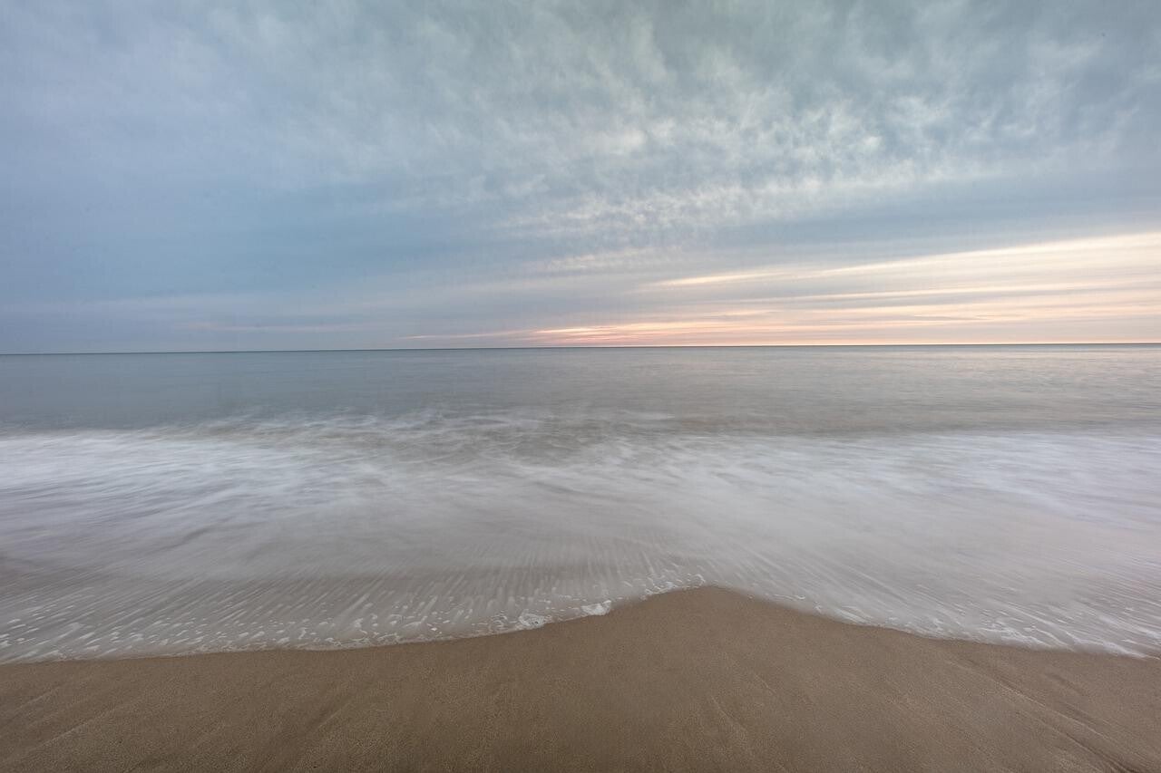 Weite Strandaufnahme mit sanftem Wellengang und bewölktem Himmel bei Sonnenuntergang, passend zum Thema Geistführerkontakt mit Medium Jana Lorenz