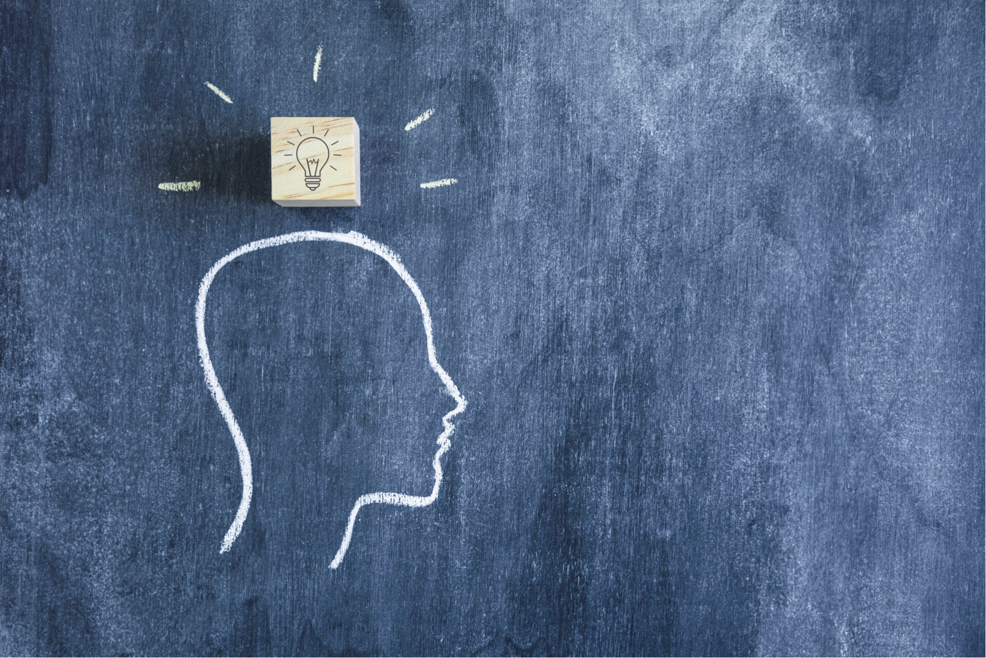 Kreidezeichnung eines menschlichen Profils auf Tafel mit Holzblock darüber, der eine Glühbirne zeigt, Symbol für Idee oder Inspiration, Kontext Blog Jenseitskontakte Jana Lorenz