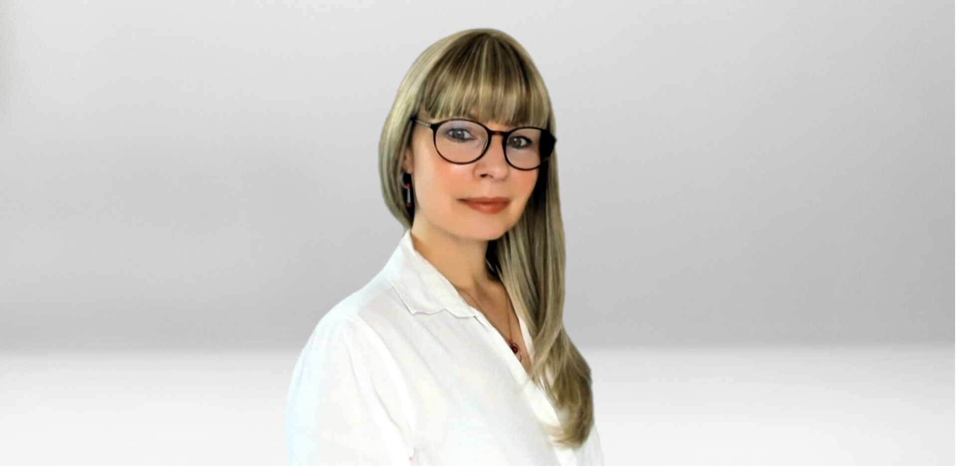 Jana Lorenz mit langen blonden Haaren, trägt weiße Bluse und goldene Ohrringe, Halskette mit rundem roten Anhänger