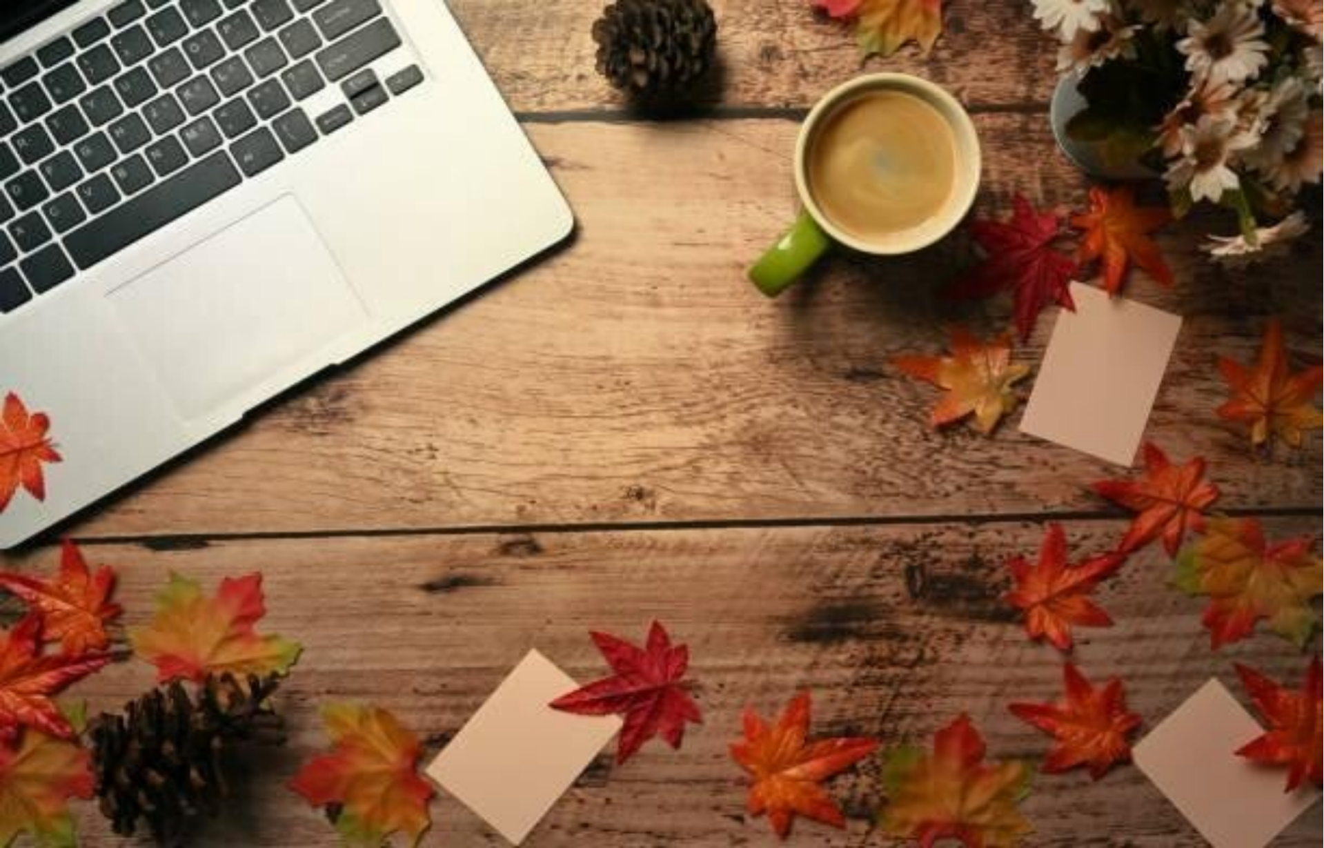 Ein Laptop und bunte Herbstblätter sind auf einem Holztisch arrangiert, was eine einladende Arbeitsumgebung schafft, im Kontext mit Jenseitskontakte Jana Lorenz.