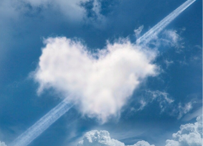 Eine herzförmige Wolke im Himmel, umgeben von weiteren Wolken und einem Kondensstreifen, Kontext Blog Jenseitskontakte Jana Lorenz.