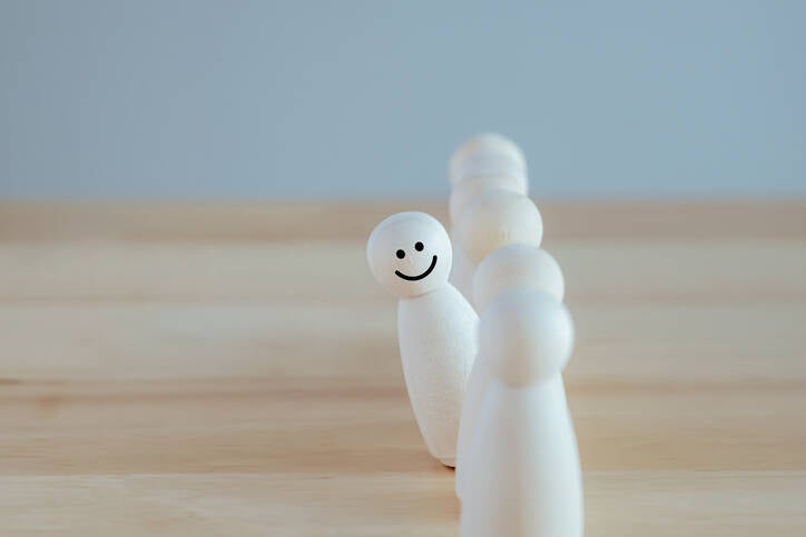 Sechs kleine, weiße Holzfiguren stehen auf einem Tisch. Eine Figur hat ein lächelndes Gesicht, die anderen sind neutral, Kontext Blog Jenseitskontakte Jana Lorenz.