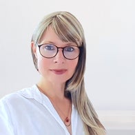 Jana Lorenz mit langen blonden Haaren, trägt weiße Bluse und goldene Ohrringe, Halskette mit rundem roten Anhänger