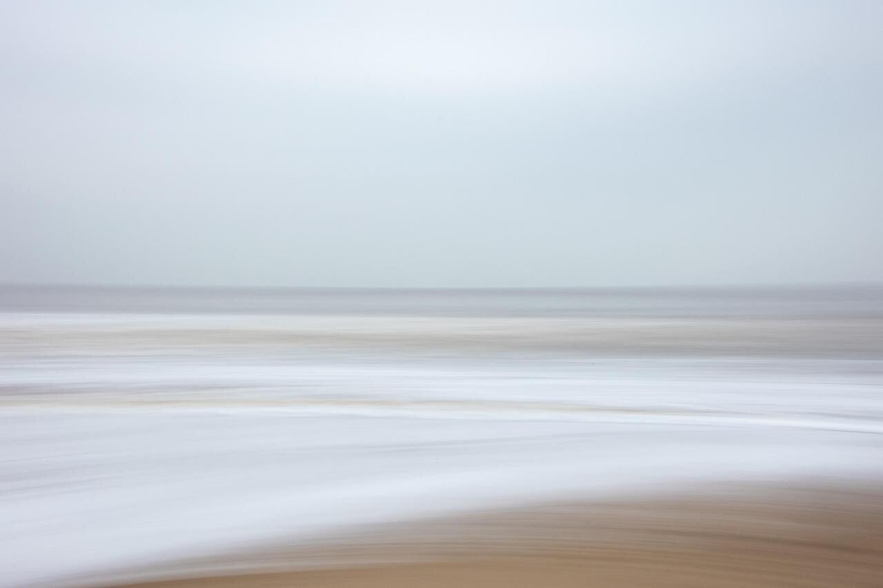 unscharfe Aufnahme eines Sandstrands mit Wellen und Horizont, passend zum Thema Geistführerkontakt mit Medium Jana Lorenz