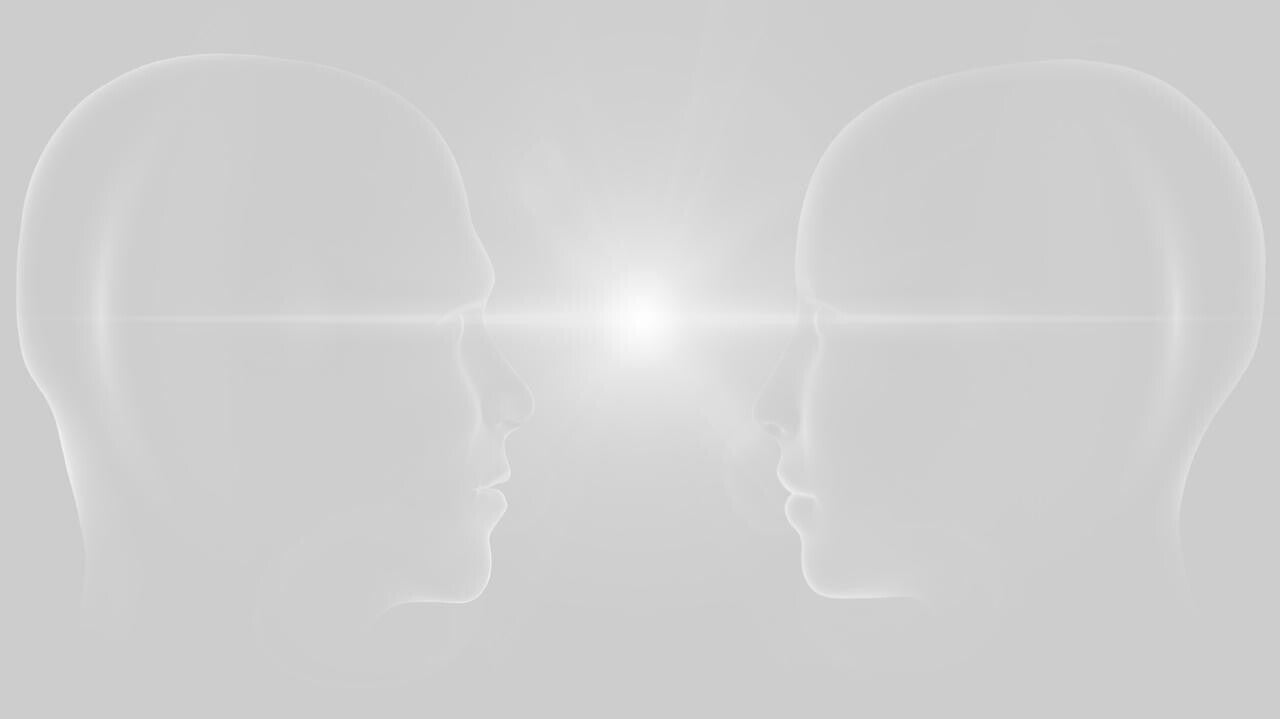 Zwei stilisierte, durchsichtige Köpfe in Profilansicht, die sich gegenüberstehen. Zwischen ihnen strahlt ein heller Lichtpunkt, Kontext Blog Jenseitskontakte Jana Lorenz.