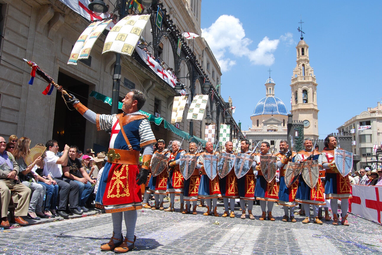 Cabo y escuadra de la filà Navarros, con escudos de la cruz, durante la Entrada Cristiana de los Moros y Cristianos de Alcoy, con el público sentado a los lados.