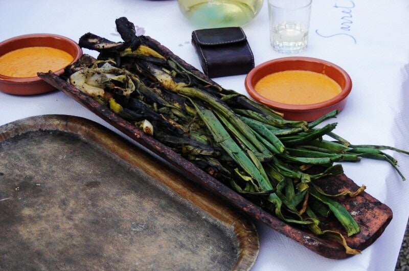 Calçots asados a la brasa, ennegrecidos por fuera, junto a un cuenco de salsa romesco para mojarlos