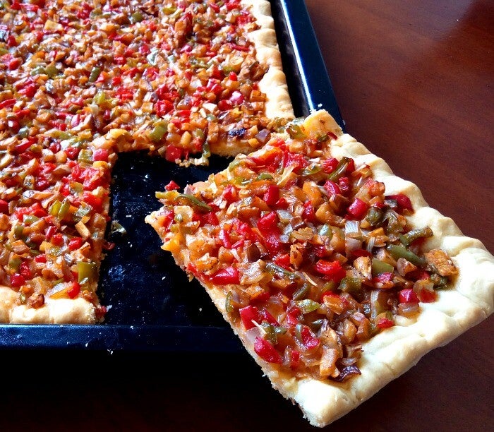 Coca de trampó balear, masa fina con tomate, cebolla y pimiento verde crudos.