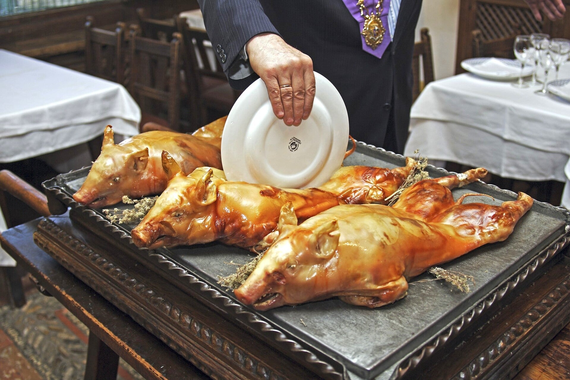 Hombre cortando un cochinillo asado tradicional de Segovia con la técnica propia del corte con plato