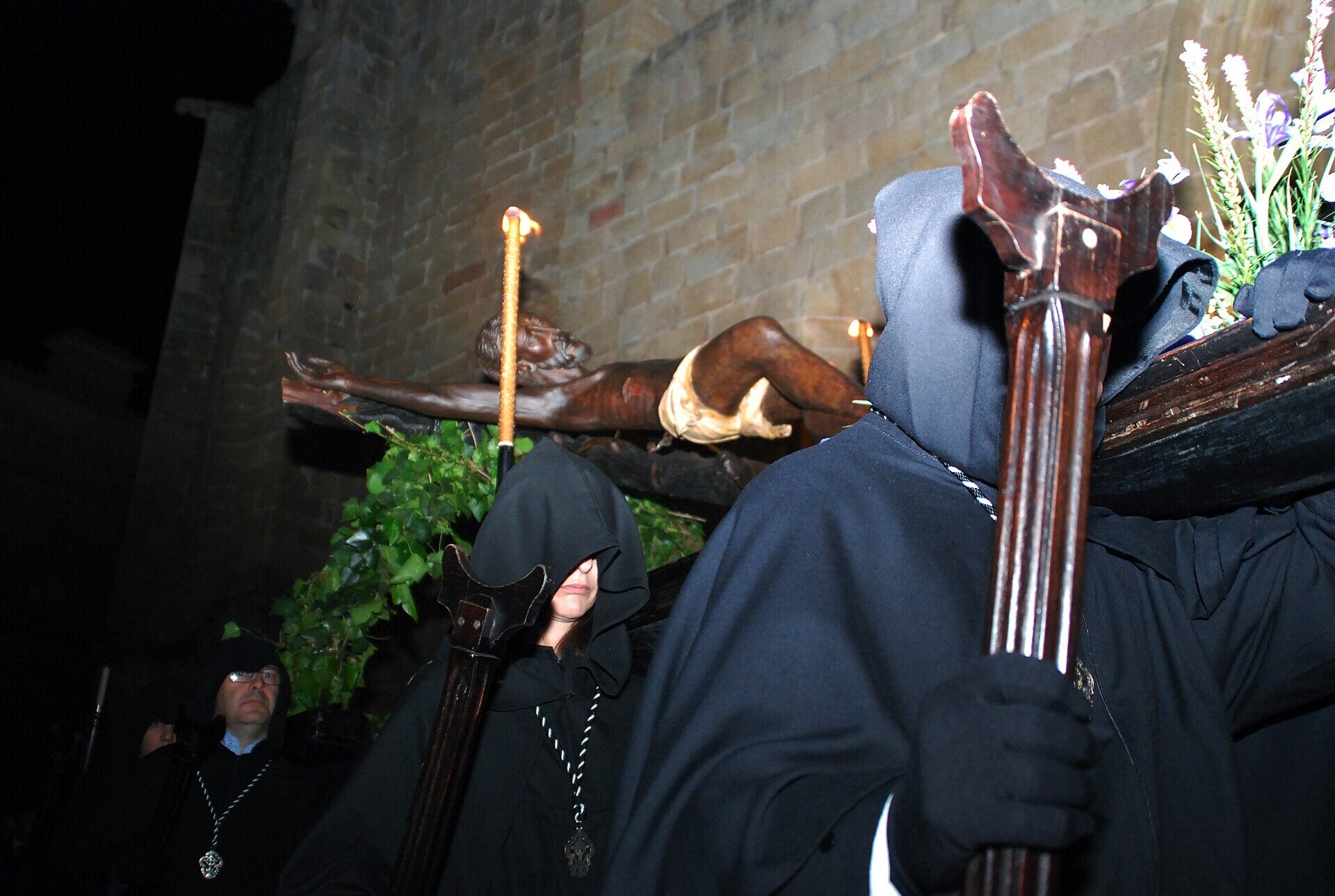 Hermano encapuchado con hábito negro junto al Cristo Negro en su procesión de medianoche en la Semana Santa de Cáceres