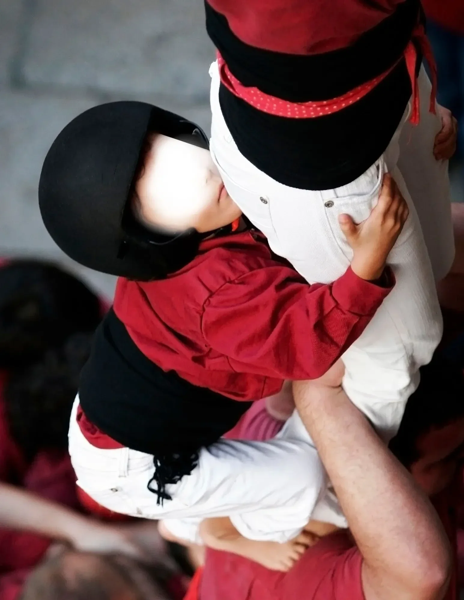 Enxaneta trepando por el tronco de un castell, agarrándose a la faixa y los hombros de los castellers