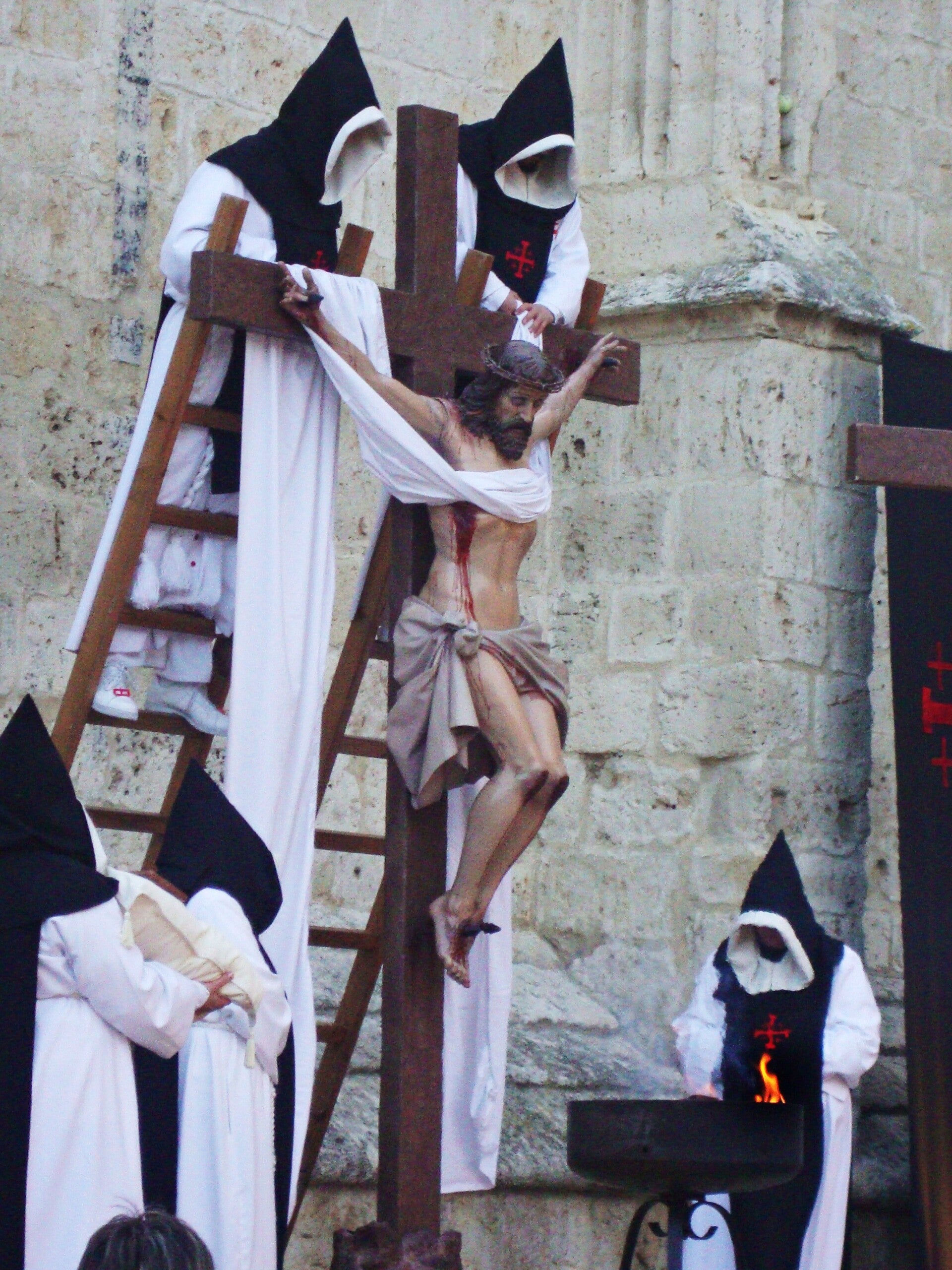 Monjes de hábito blanco y capucha negra bajan a Cristo de la cruz con una sábana desde la escalera, en la Función del Descendimiento, ante los muros de piedra de la catedral de Palencia, en su Semana Santa.