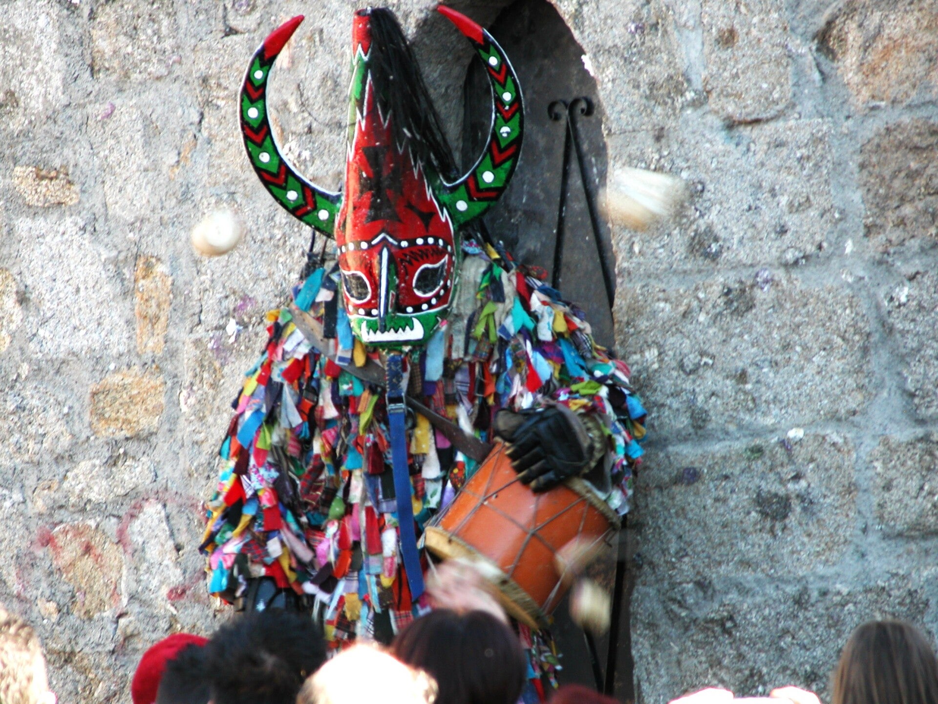 Jarramplas, con máscara de cuernos y traje de cintas de colores, junto al campanario de Piornal (Cáceres)
