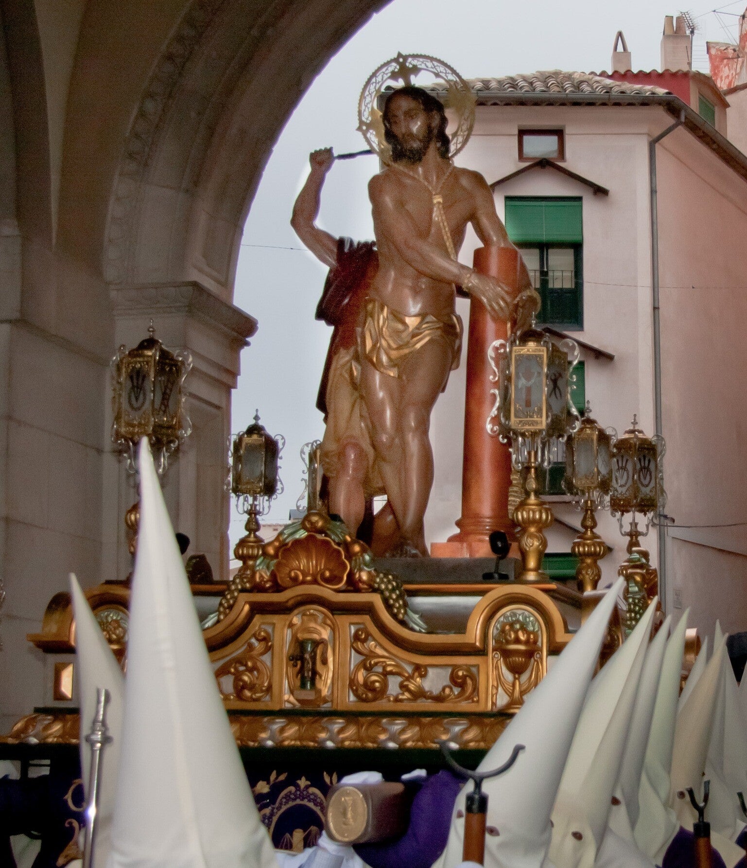 Paso de Jesús Amarrado a la Columna bajo el arco del Ayuntamiento de Cuenca, entre nazarenos de capirote blanco