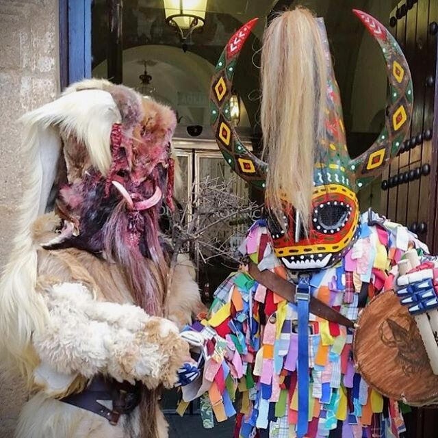 Un Jarramplas de Piornal, con máscara de cuernos y traje de cintas, junto a una Carantoña de Acehúche, fiestas hermanas