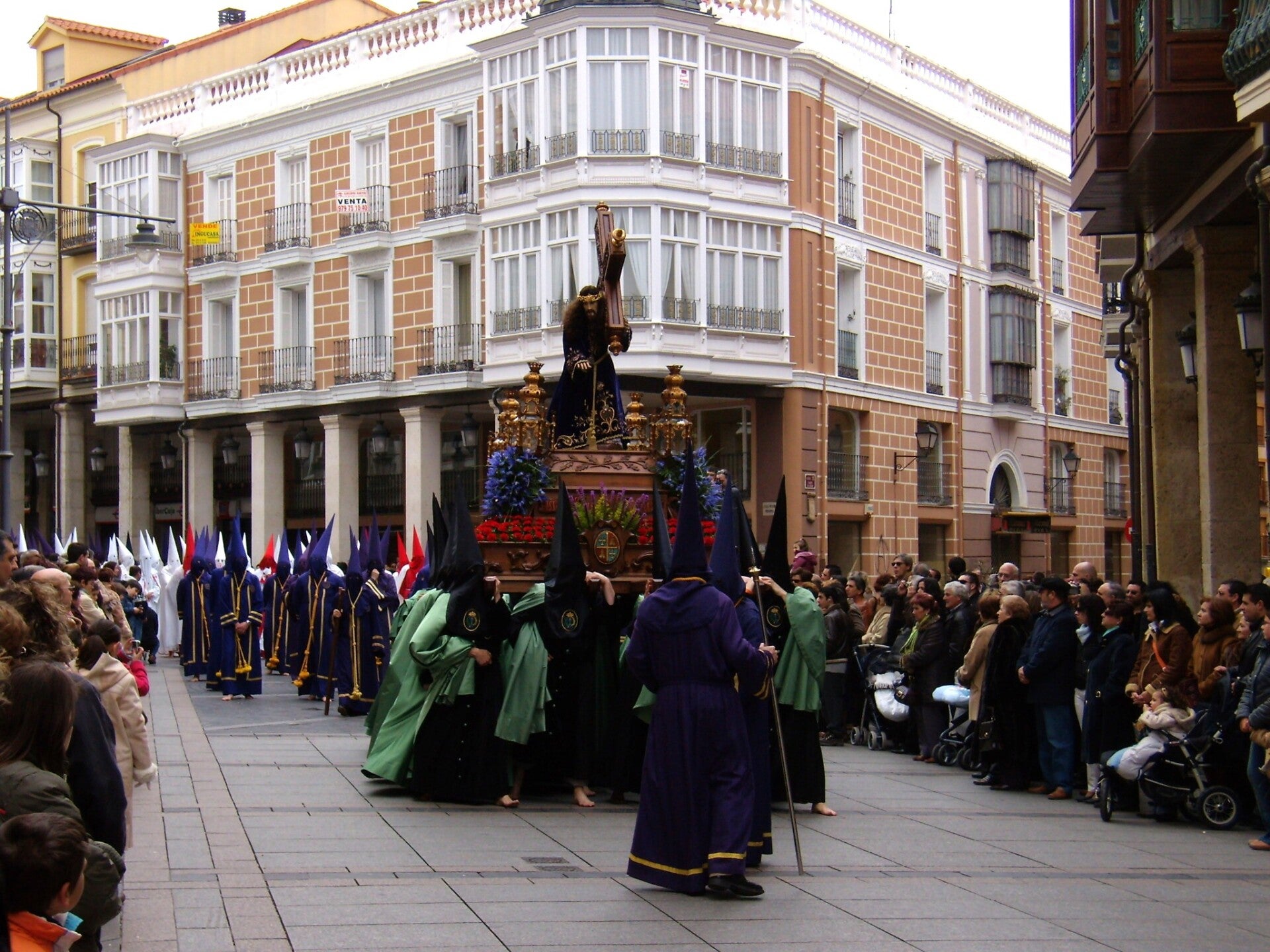Paso de Nuestro Padre Jesús Nazareno, talla de Tomás de Sierra de 1717, llevado a hombros por cofrades de túnica verde y negra entre nazarenos morados, ante el público de una calle en la Semana Santa de Palencia.