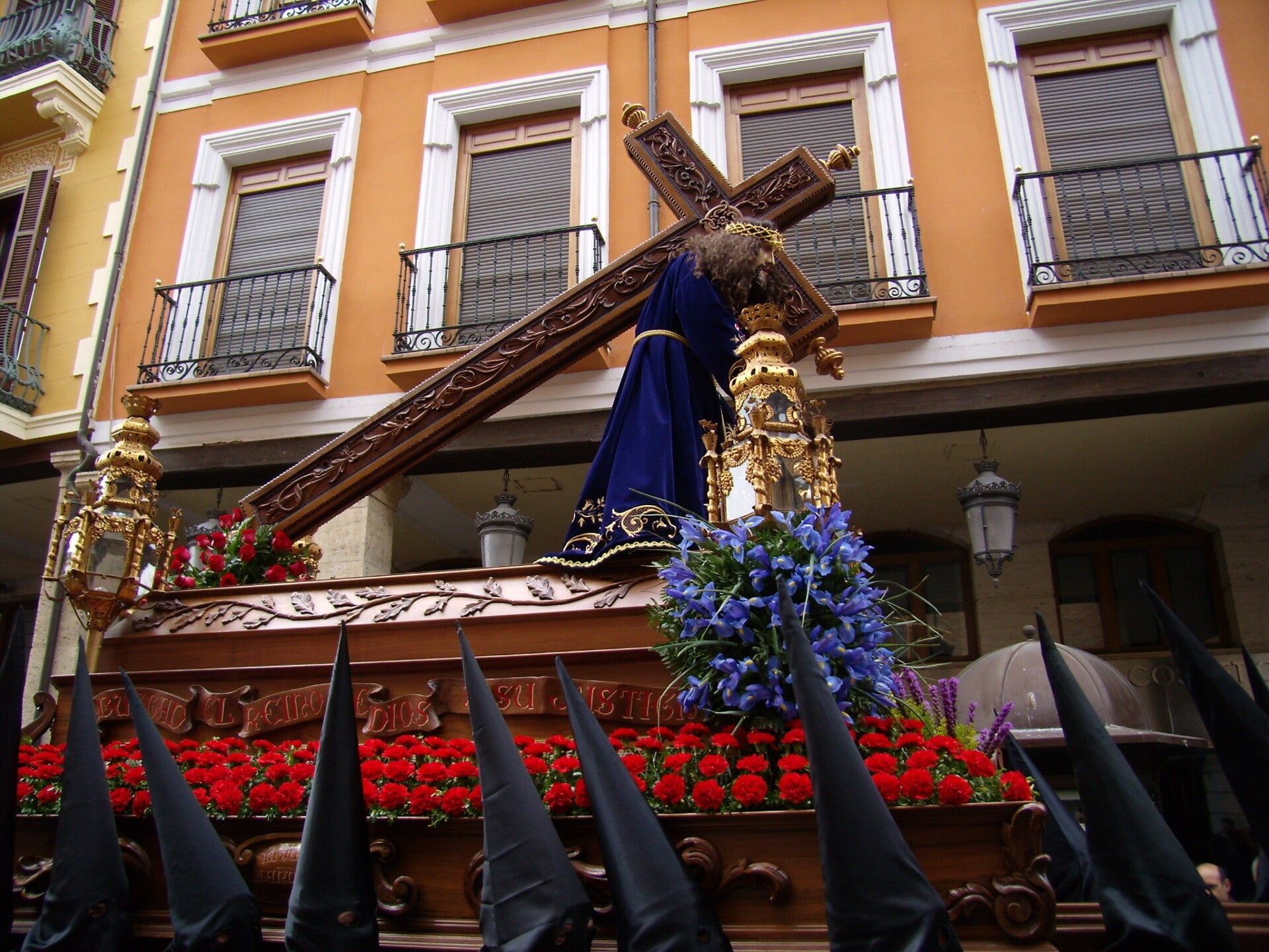 Nuestro Padre Jesús Nazareno, talla de Tomás de Sierra de 1717, con la cruz a cuestas sobre un paso de claveles rojos y flores azules, entre capirotes negros, en la Semana Santa de Palencia