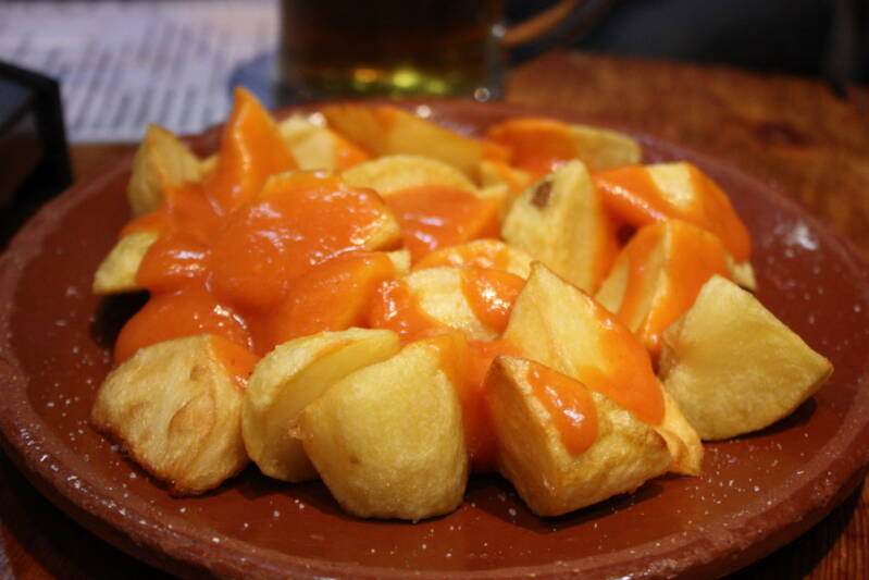Plato de patatas bravas con salsa picante roja en una barra de Madrid. 
